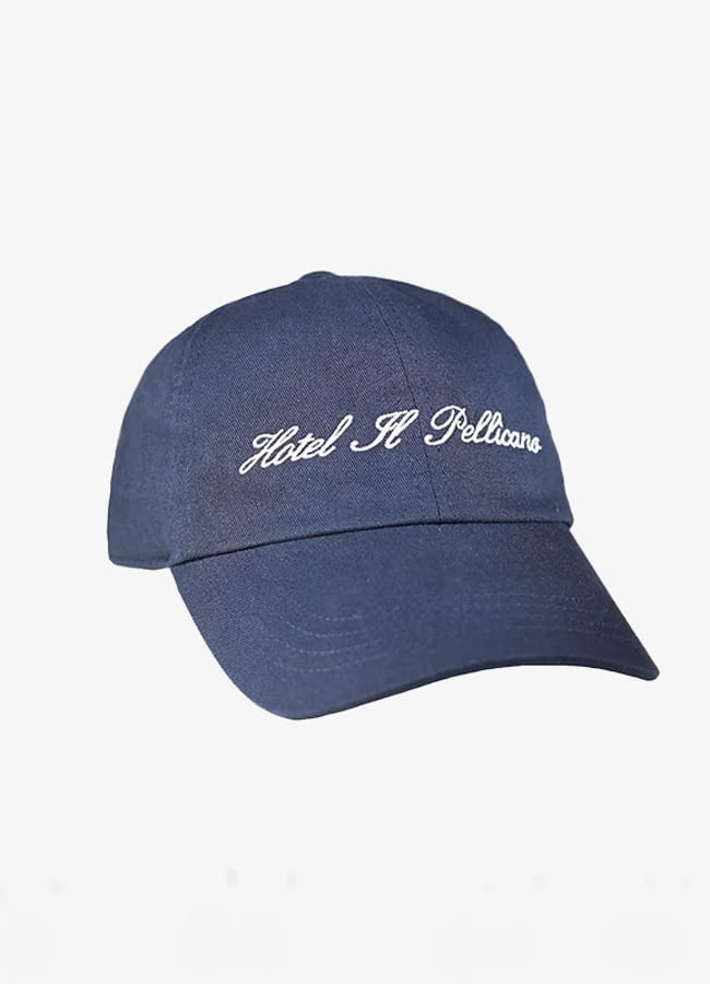 A navy blue baseball cap with white embroidered text that reads Hotel Il Pellicano on the front, displayed against a plain white background—perfect for channelling the effortless style of celebrity couples on holiday.