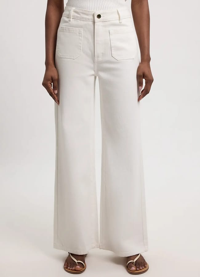 A person wearing high-waisted, wide-leg white denim jeans with front patch pockets, paired with a sleeveless white top and sandals, standing against a plain background.
