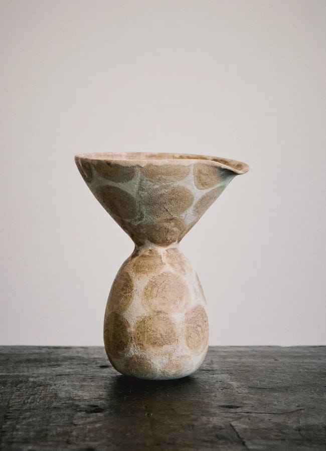 A statement vase with a wide, flared top and round base, this ceramic piece is decorated with light beige circular patterns and sits elegantly on a dark wooden surface against a plain light background.
