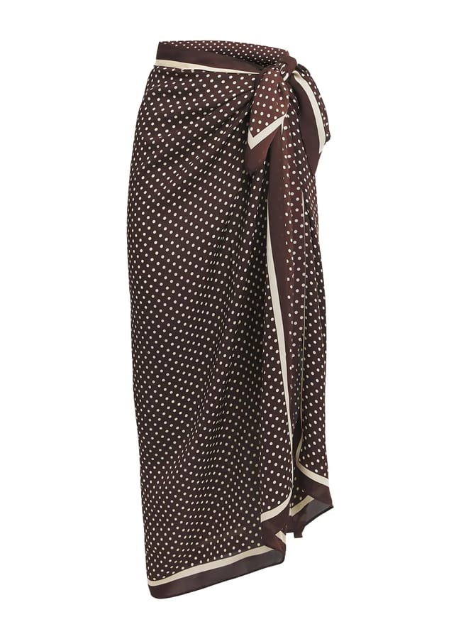 Brown maxi skirt with white polka dots, a wraparound design, and a tie at the waist. Perfect for minimalist summer fashion, the skirt features a light-coloured trim along the edges for added detail.