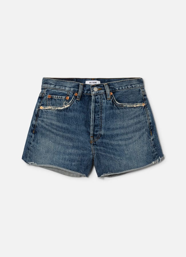 A pair of blue denim shorts with a frayed hem, front pockets, belt loops, and a button and zip fastening, displayed on a plain white background—perfect for capturing the relaxed style often seen on celebrity couples on holiday.