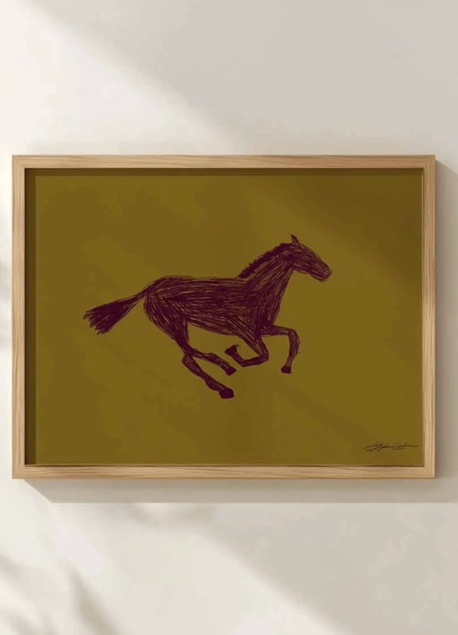 A framed minimalist drawing of a galloping horse in dark brown on a mustard yellow background, hanging on a white wall with soft shadows—a subtle nod to the chartreuse colour trend that’s making waves in modern interiors.