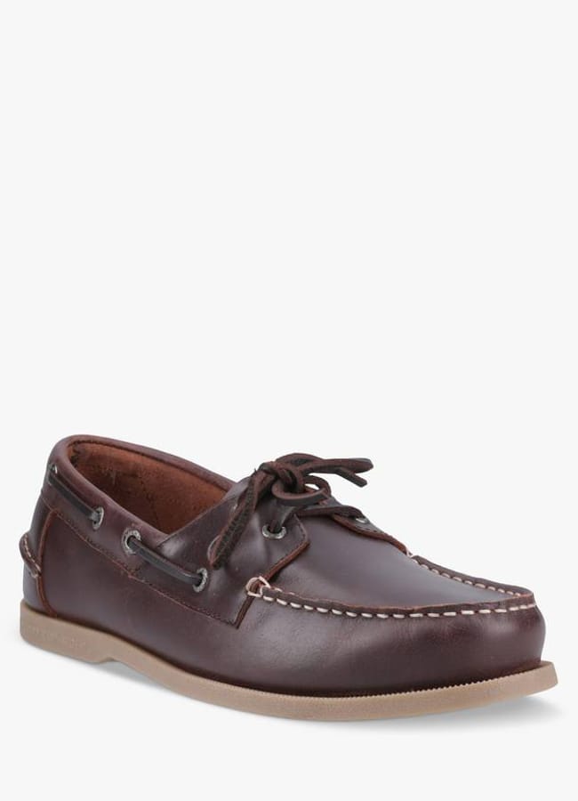 A single brown leather boat shoe with white stitching, side lacing details, and a light brown rubber sole is shown facing slightly to the right on a white background—a stylish choice reminiscent of the relaxed fashion often spotted on celebrity couples on holiday.