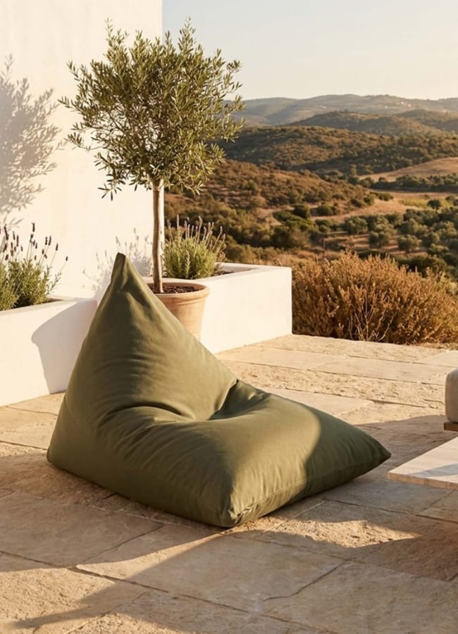A green beanbag sits on a stone patio beside a potted tree, overlooking rolling hills and dry landscape under warm sunlight—the perfect setting for an outdoor film night at home.