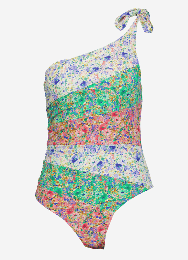 A one-shoulder swimming costume with a side tie and a multicoloured floral pattern in horizontal stripes of white, purple, green, red, and blue on a white background—this pretty swimwear is perfect for making a stylish splash.