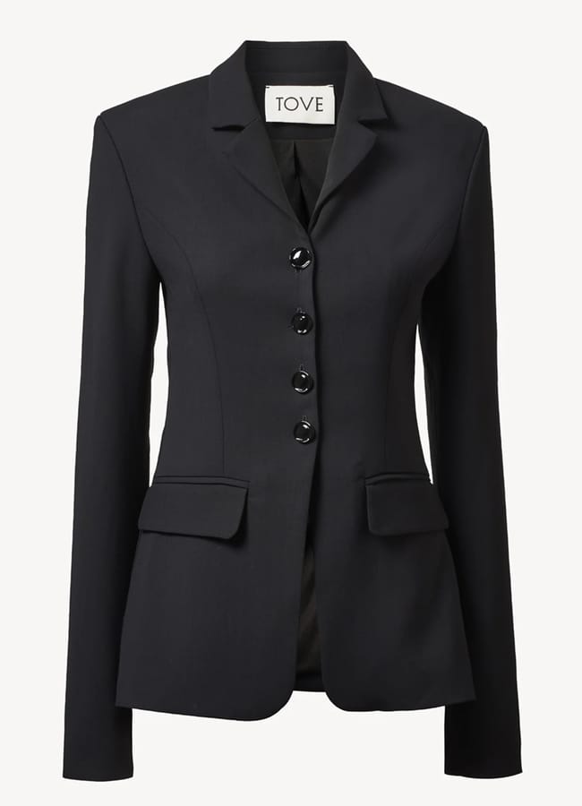 A tailored black blazer with four buttons, two front flap pockets, and a notched collar. The label inside reads TOVE—now available in our exclusive Summer Sale.