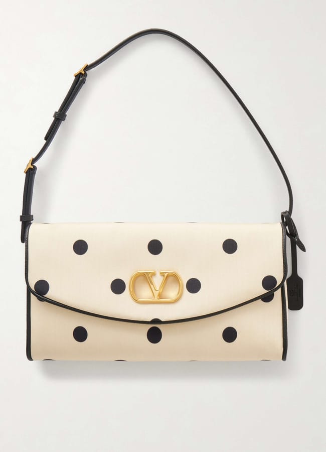 A white handbag with black polka dots, a gold logo clasp in the centre, black trim, and a black adjustable shoulder strap—this chic accessory is perfect for elevating your holiday style with a touch of celebrity fashion.
