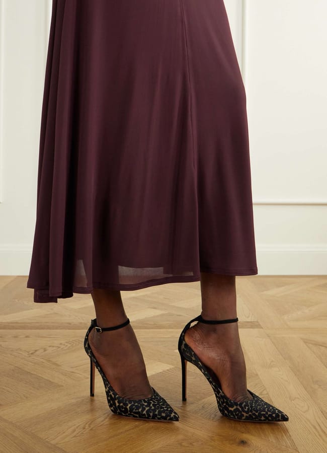A person wearing a dark burgundy midi dress and sexy heels with a leopard print stands on a wooden floor.