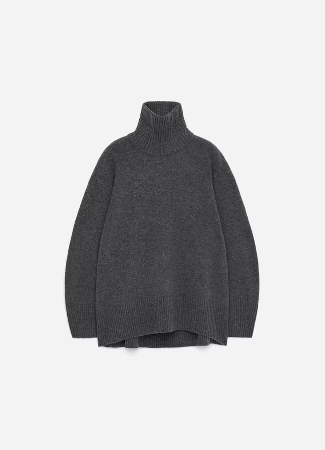 A dark grey, long-sleeved, oversized polo-neck jumper with ribbed cuffs, hem, and collar—reminiscent of pieces found in minimalist high street brands—laid flat on a light background.