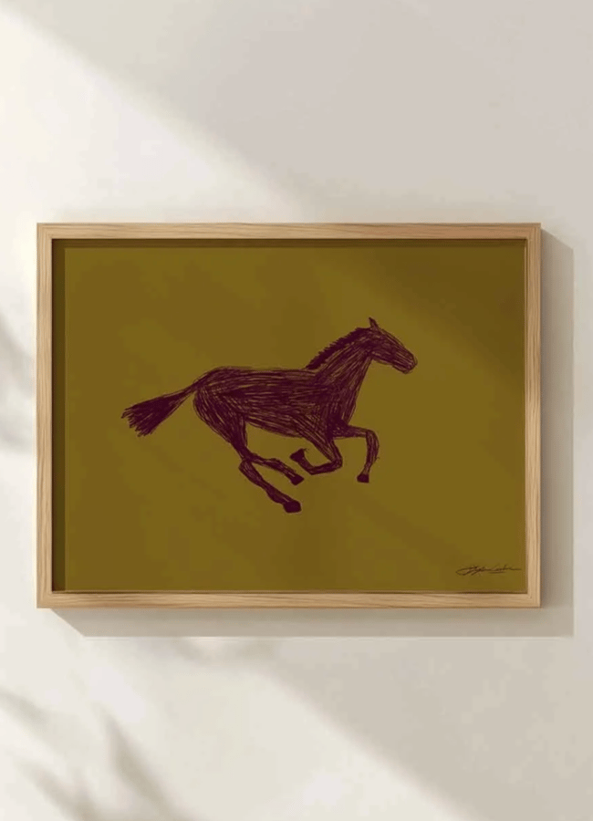 A framed artwork depicts a galloping horse in dark brown lines on an olive green background, showcasing unexpected colours and stylish colour combinations. It hangs on a light-coloured wall with soft shadows, creating a contemporary visual appeal.