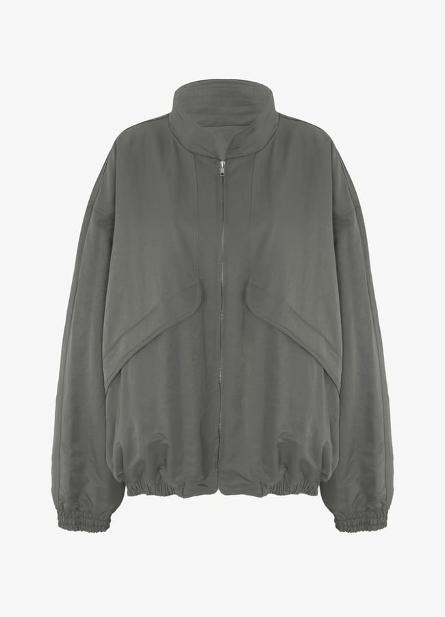 A grey zip-up jacket with a high collar, dropped shoulders, elasticated cuffs, and a loose fit. This stylish piece—perfect for fans of lightweight jackets—features curved seam details across the front and an elasticated hem.
