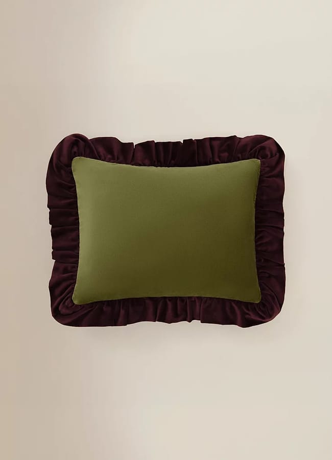 A rectangular olive green cushion with a dark purple frilled border, placed on a plain light beige background—a perfect example of chic homeware under £50.