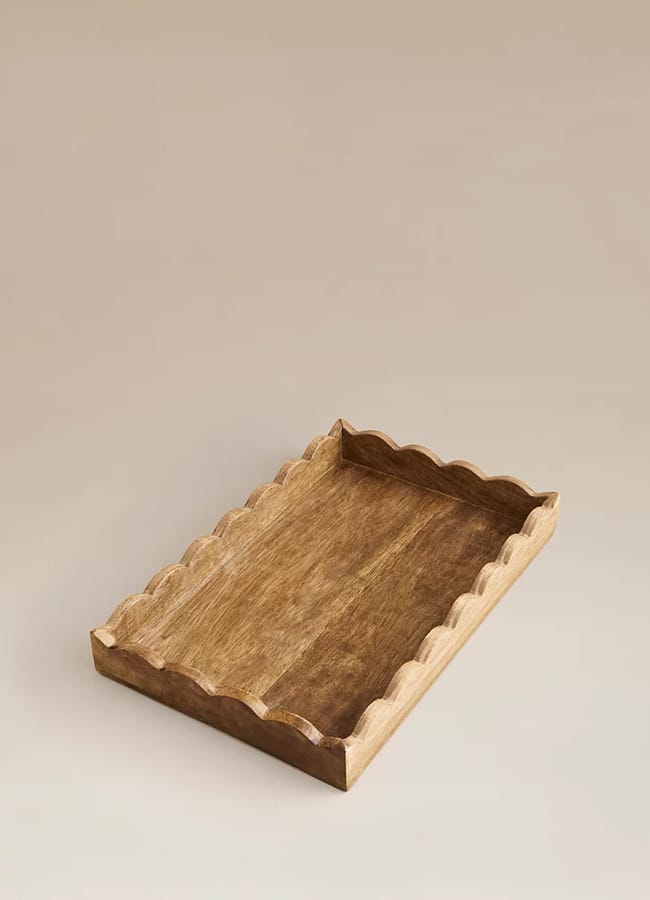 A rectangular wooden tray with raised, scalloped edges on all sides, placed on a neutral, light-coloured surface—a perfect piece of chic homeware under £50.