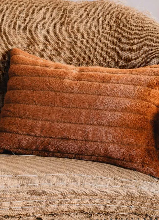 A brown faux fur cushion rests on a textured, tan hessian sofa with visible stitching and a curved back—an inviting addition to any space, perfect for those seeking chic homewares under £50.