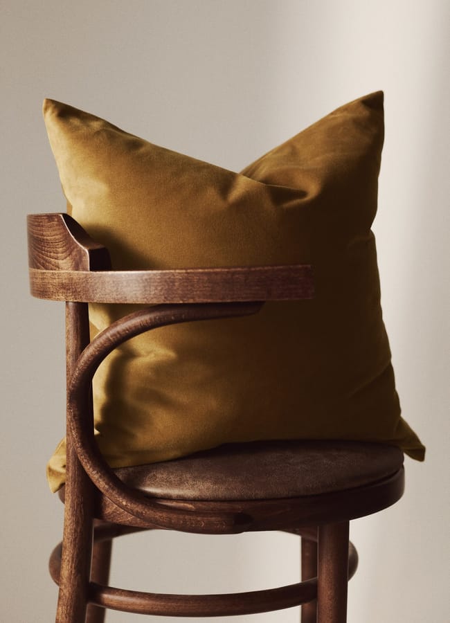 A mustard yellow cushion rests on a vintage wooden chair with a curved back, in soft, natural light—a perfect accent for any caramel homeware collection.