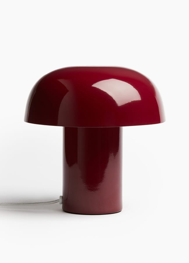 A modern table lamp with a glossy, deep red mushroom-shaped design sits on a white background. Perfect for adding personality to any room, this chic homeware under £50 features a thin, white power lead that extends from its base.