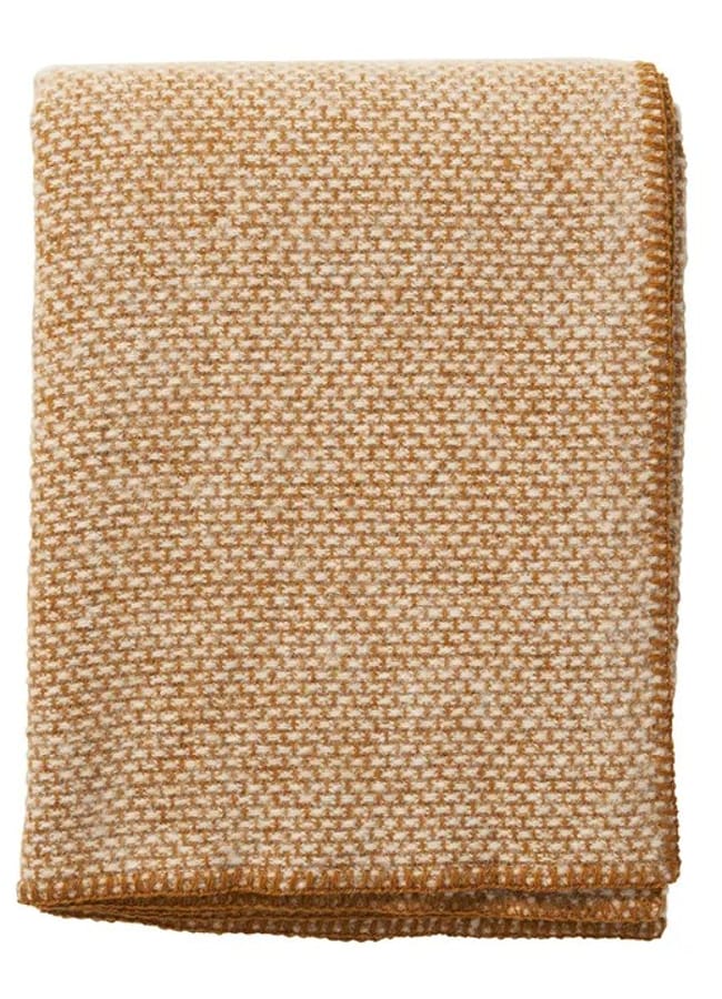 A folded, textured blanket with a small, checked pattern in tan and off-white hues—perfect for elevating your caramel homeware collection—neatly stacked against a plain white background.