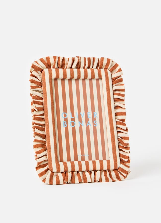 A rectangular photo frame with ruffled, orange and white striped fabric around the edges, displaying the text OLIVER BONAS on striped paper inside—perfect for adding a pop of colour to your décor and a stylish choice in chic homeware under £50.