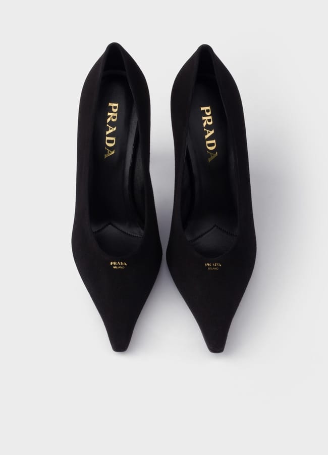 A pair of sexy black Prada high-heeled shoes seen from above on a white background, showing the gold Prada logo printed on the insoles.