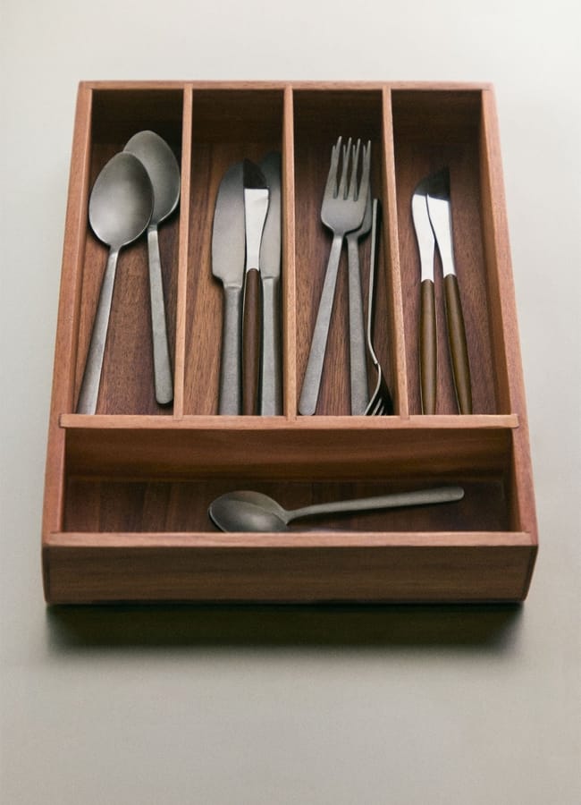 A chic homeware under £50, this wooden cutlery tray features neatly organised compartments holding spoons, knives, and forks, with an extra spoon placed in front on a light surface.