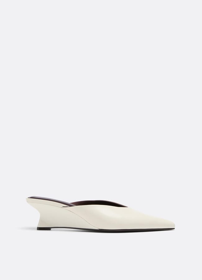 A minimalist, off-white mule shoe with a pointed toe and a low, angled wedge heel—reminiscent of styles seen in leading minimalist high street brands—displayed on a plain light background.