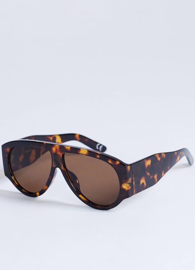 Tortoiseshell-patterned sunglasses with large, round brown lenses are resting on a plain white surface—an effortless addition to your style essentials and perfect for those seeking subtle wardrobe upgrades.