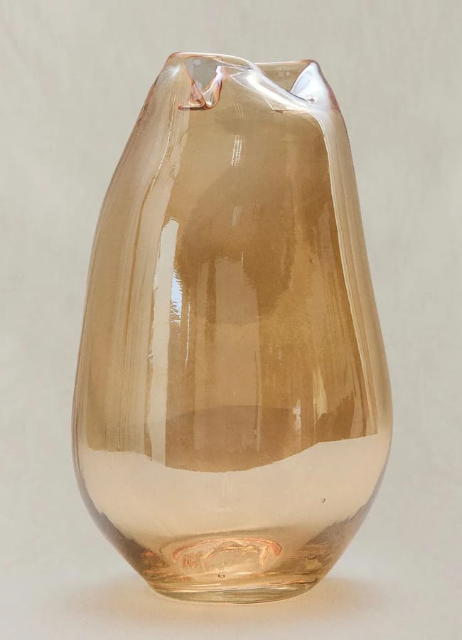 A translucent, amber-coloured glass vase with an irregular, organic shape and a slightly crumpled top sits against a plain, light background—a striking example of caramel homeware that brings warmth and sophistication to any space.