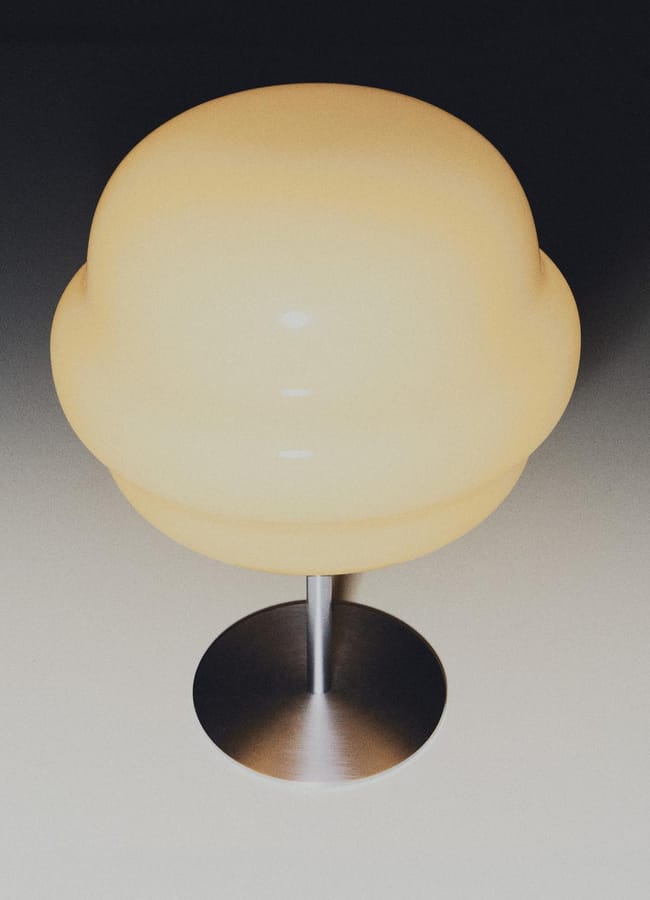 A modern table lamp with a round, opaque white shade and a metallic base, photographed from above against a neutral background—an ideal choice for those seeking chic homeware under £50.