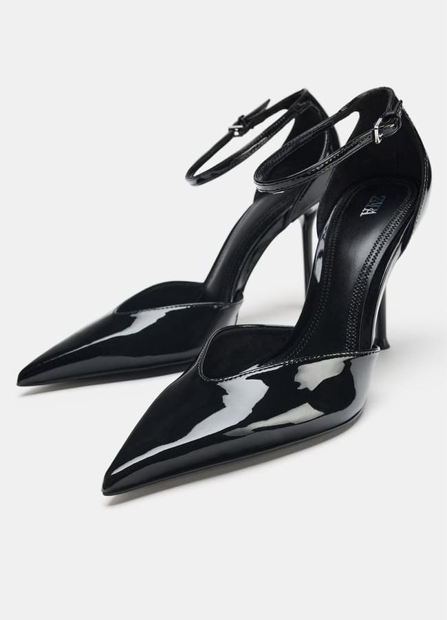 Glossy black pointed-toe sexy heels with ankle straps and thin stiletto heels, displayed against a plain white background.