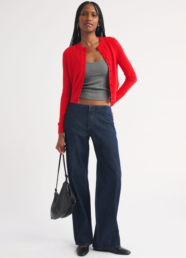 A person wearing a cropped red cardigan over a grey vest and wide-leg dark-wash jeans, carrying a black handbag.