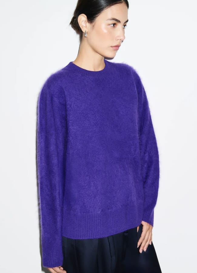 A person wears a long-sleeved, purple crew-neck jumper.
