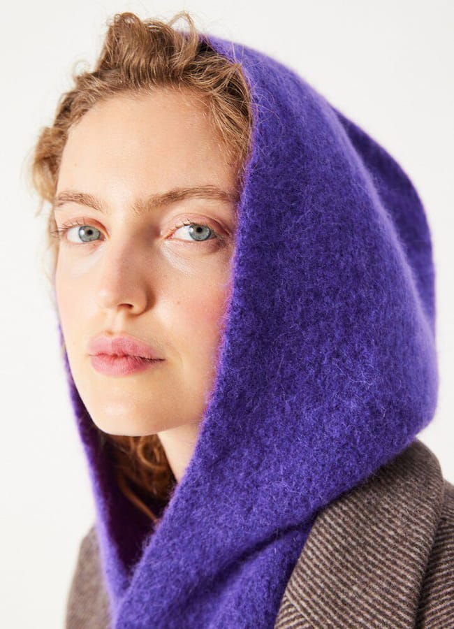 A person wearing a purple hooded garment layered over a brown striped coat.