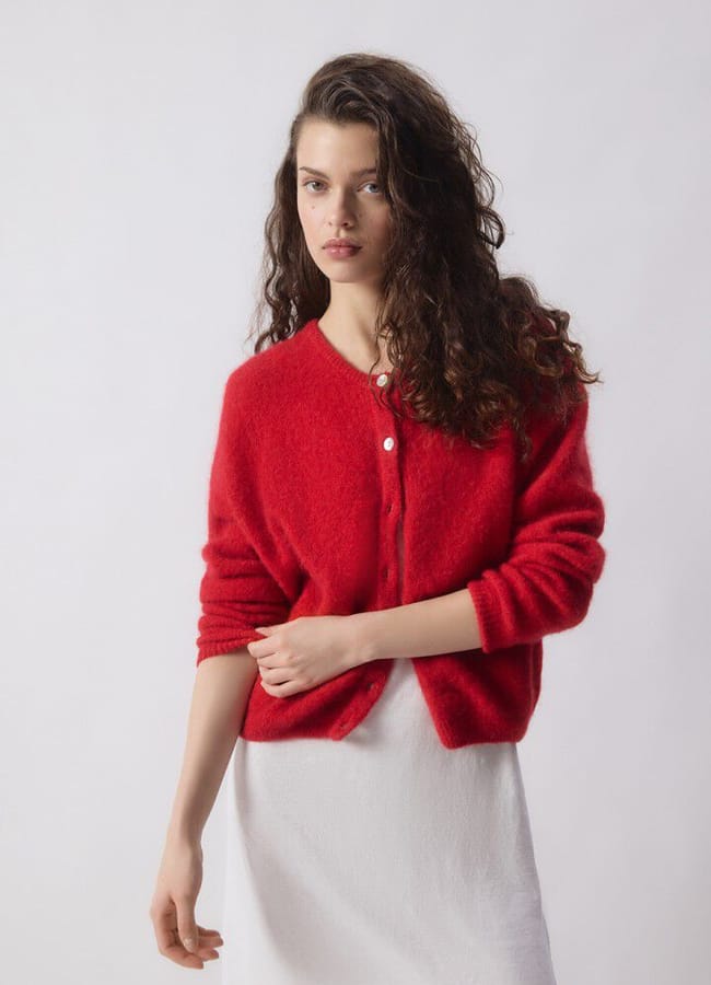 A woman wearing a cropped red cardigan over a white dress.
