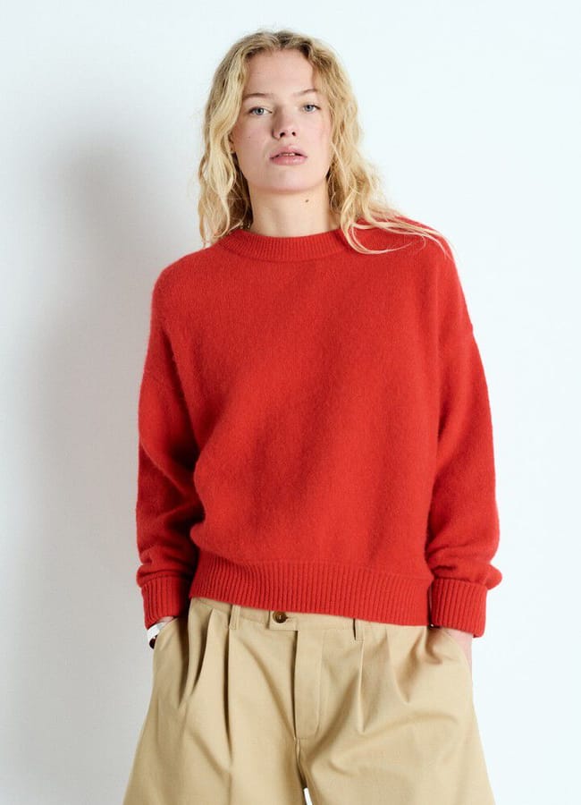 A person wearing a crew-neck red jumper and beige pleated trousers.