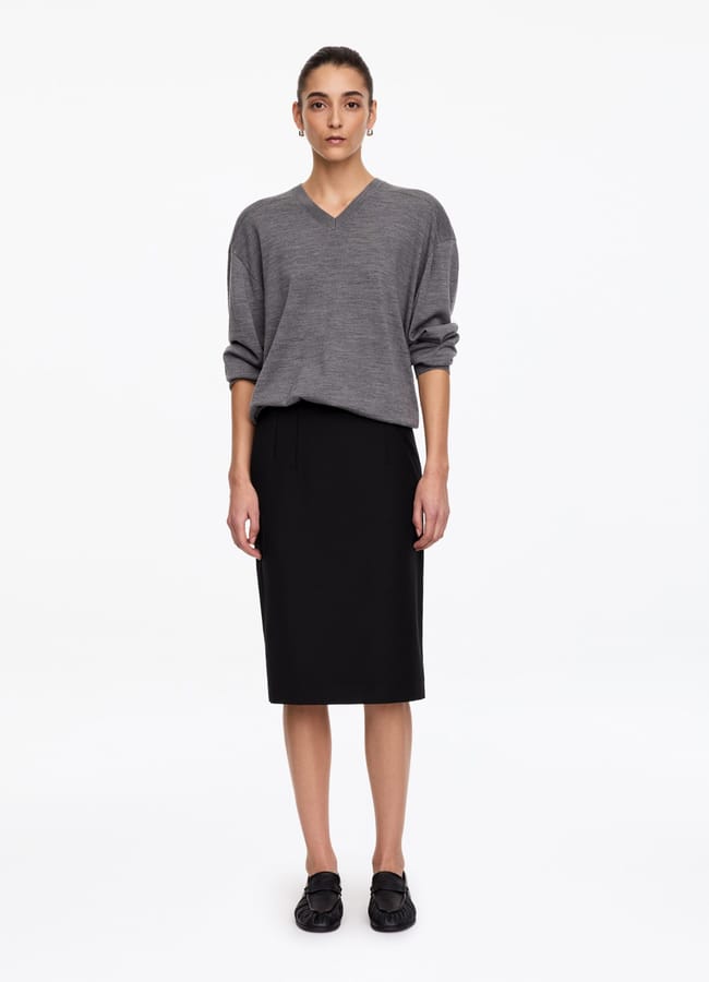 A model wearing a grey V-neck jumper, a black knee-length pencil skirt, and black loafers.