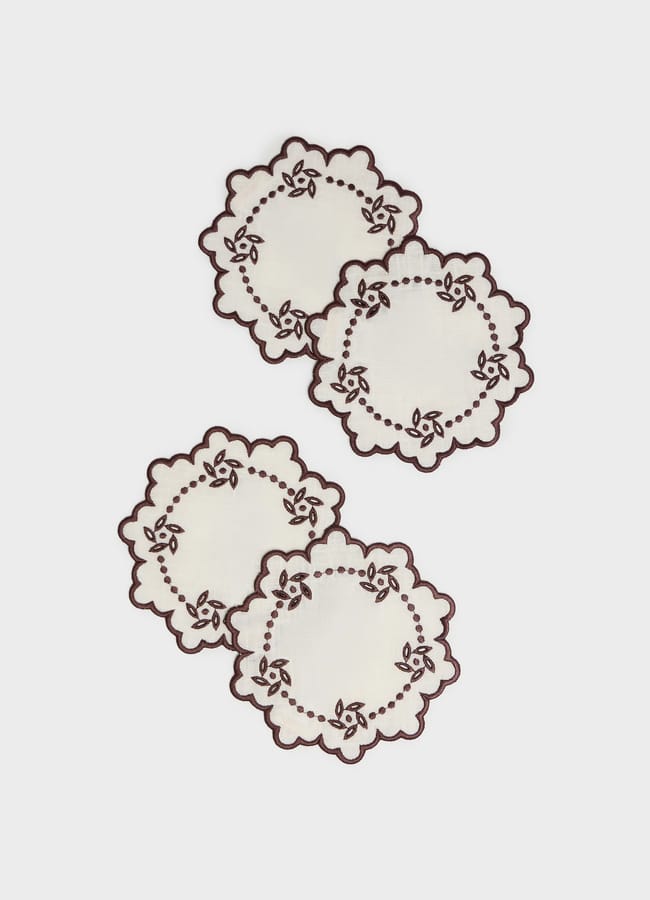 Four round, off-white coasters with scalloped edges and dark brown floral embroidery, perfect for autumn tablescape ideas.