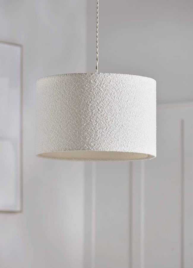A cylindrical, textured white bouclé pendant light fitting hanging from a flex.