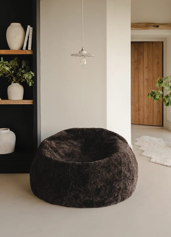 A dark brown textured beanbag chair in a minimalist listening room, with a black shelving unit and a wooden door in the background.
