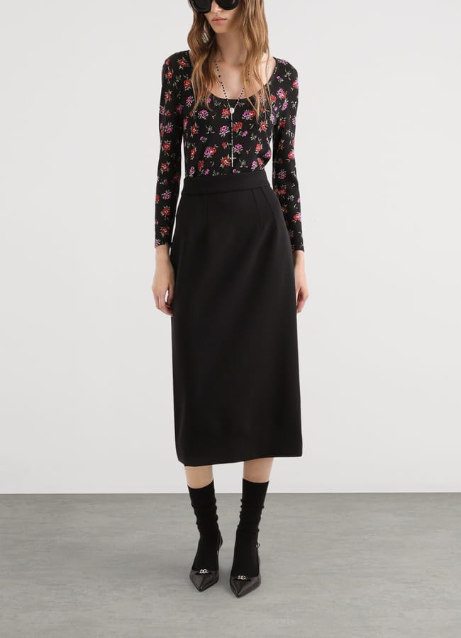 A person wearing a long-sleeved floral top, a black midi pencil skirt, black socks, and black heels.