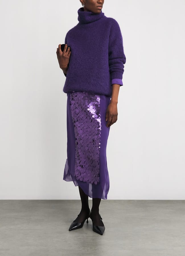 A person wearing a purple polo-neck jumper over a midi skirt with a central panel of large purple sequins.