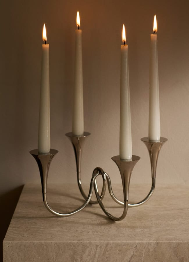 A silver four-armed candelabra holding four lit white taper candles, serving as a centrepiece for autumn tablescape ideas.