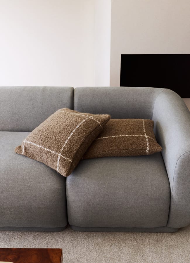 Two brown, textured bouclé cushions with a white grid pattern resting on a light grey sofa.