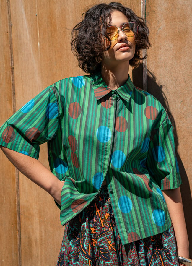 A person wears a patterned skirt paired with a green short-sleeved shirt featuring vertical stripes and large blue and brown polka dots, showcasing style from black owned fashion brands.