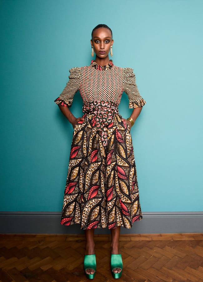 A model wears a calf-length dress from a black-owned fashion brand, featuring a patterned bodice, a leaf-print skirt, and green platform heels.