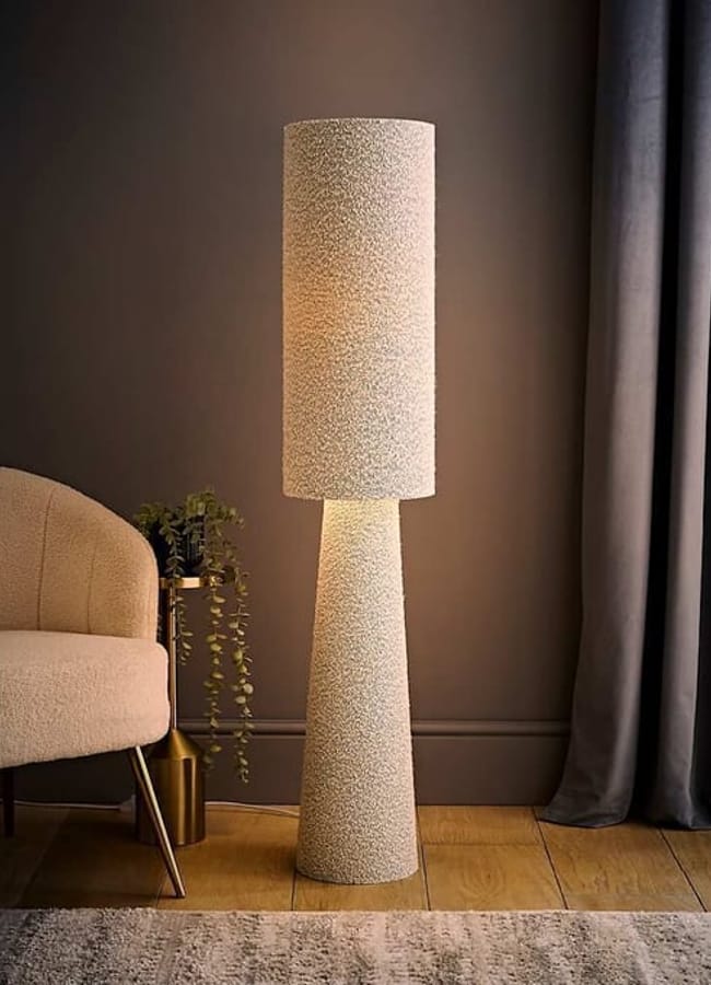A tall, cylindrical floor lamp with a textured, speckled bouclé finish, illuminated from within.