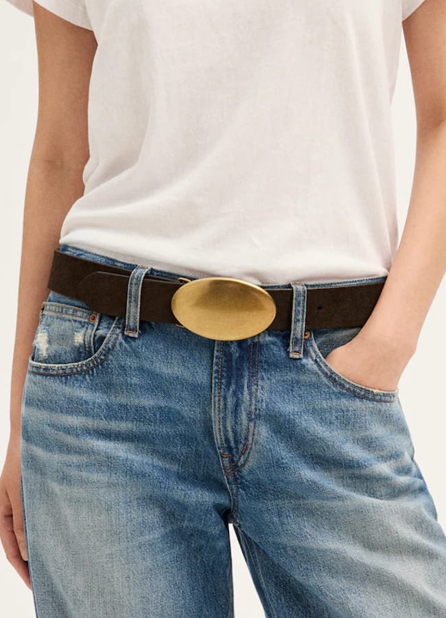 Dark brown belt with a large, oval, brushed gold buckle worn with a white T-shirt and blue jeans.