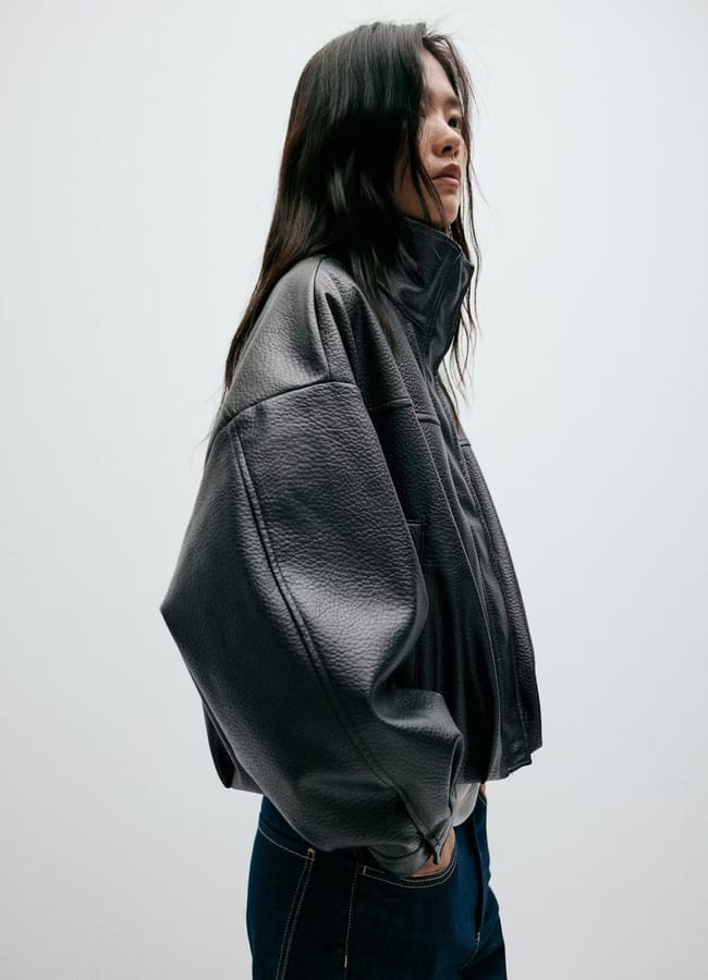 A person wearing one of the best women's leather jackets in an oversized black style with a high collar and blue jeans.