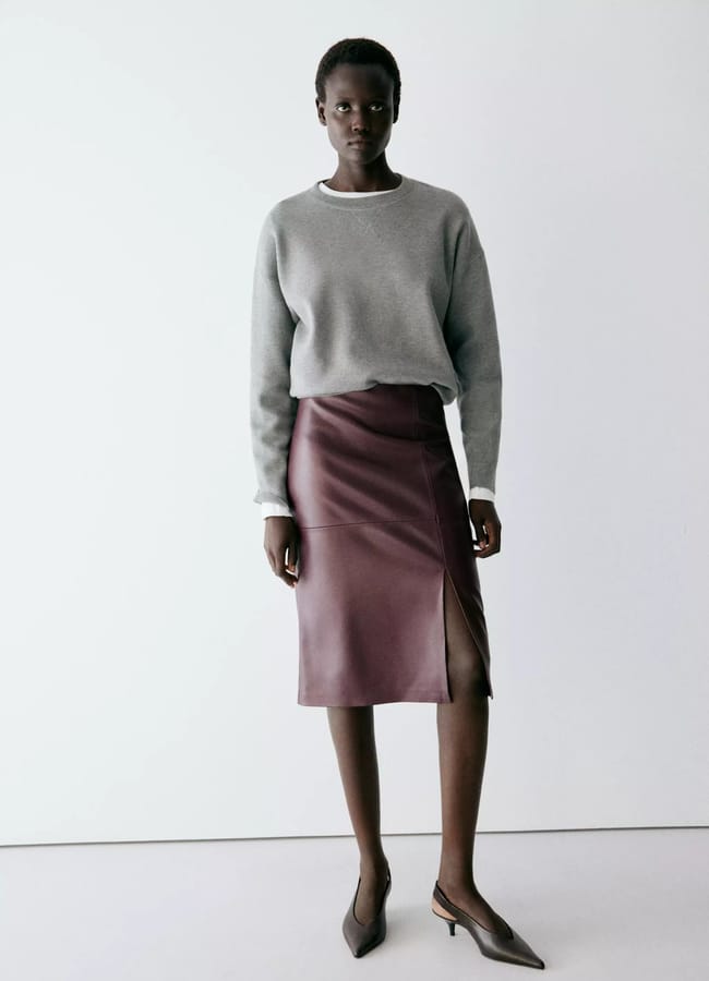 A person wearing a grey crew-neck jumper, a burgundy knee-length pencil skirt with a side slit, and dark brown slingback heels.