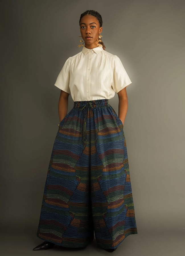 A person wearing a short-sleeved cream button-through shirt and wide-leg patterned trousers from a black-owned fashion brand.