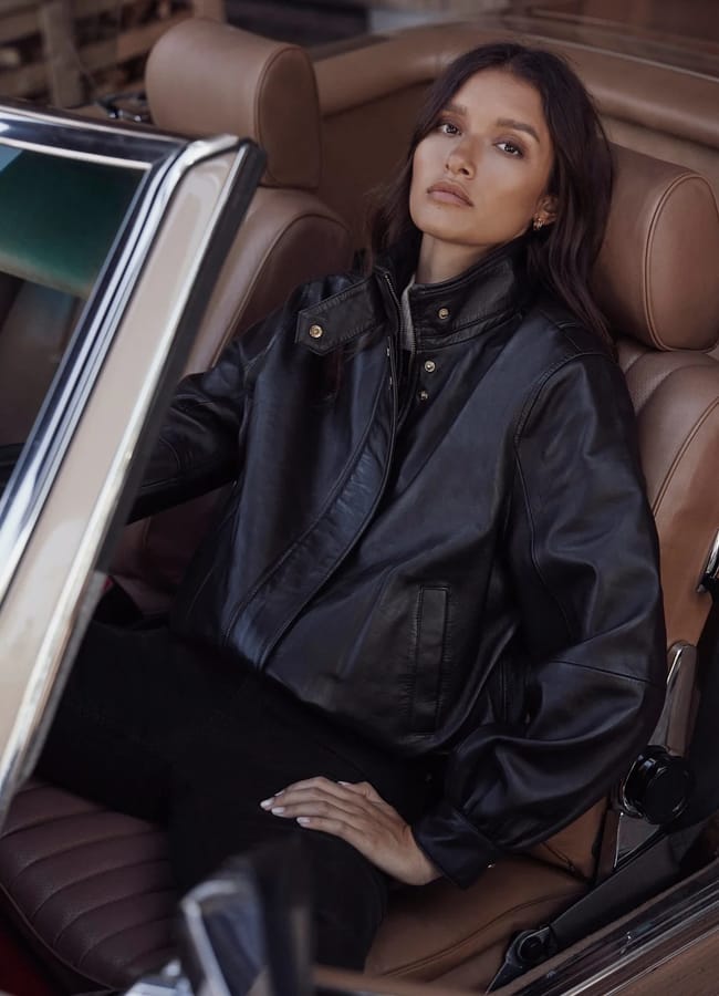 A woman wearing one of the best women’s leather jackets sits in the driver’s seat of a vintage convertible car.